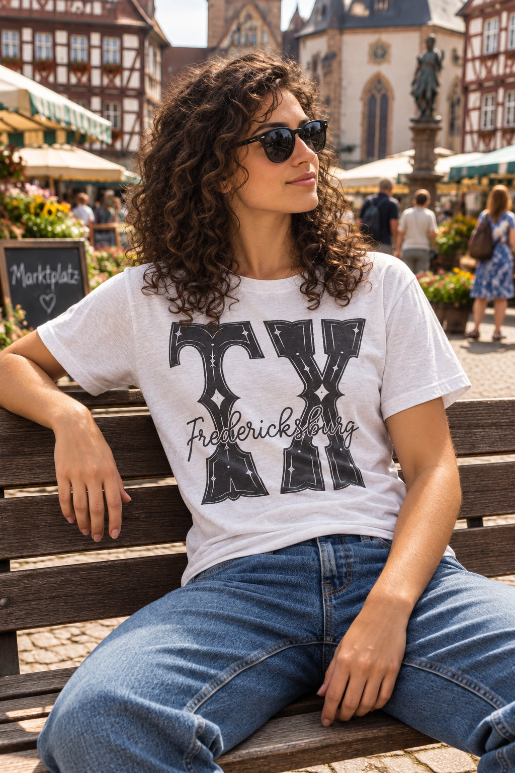 A white short-sleeve T-shirt. The shirt features a large black graphic on the front with the words 'TX' in a stylized font and 'Fredericksburg' written across the chest.