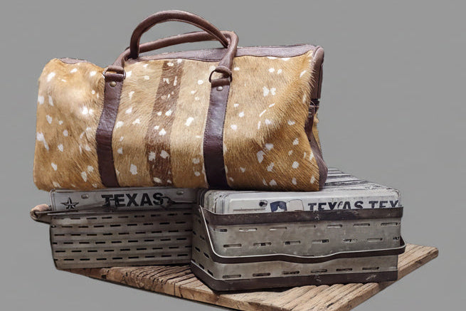 A brown and tan cowhide duffle bag with white speckles and dark brown leather handles.