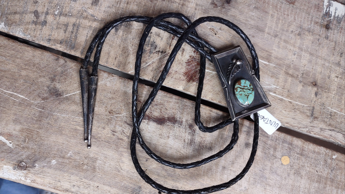 A vintage-style black braided bolo necklace with a square black pendant featuring a turquoise stone inlay.