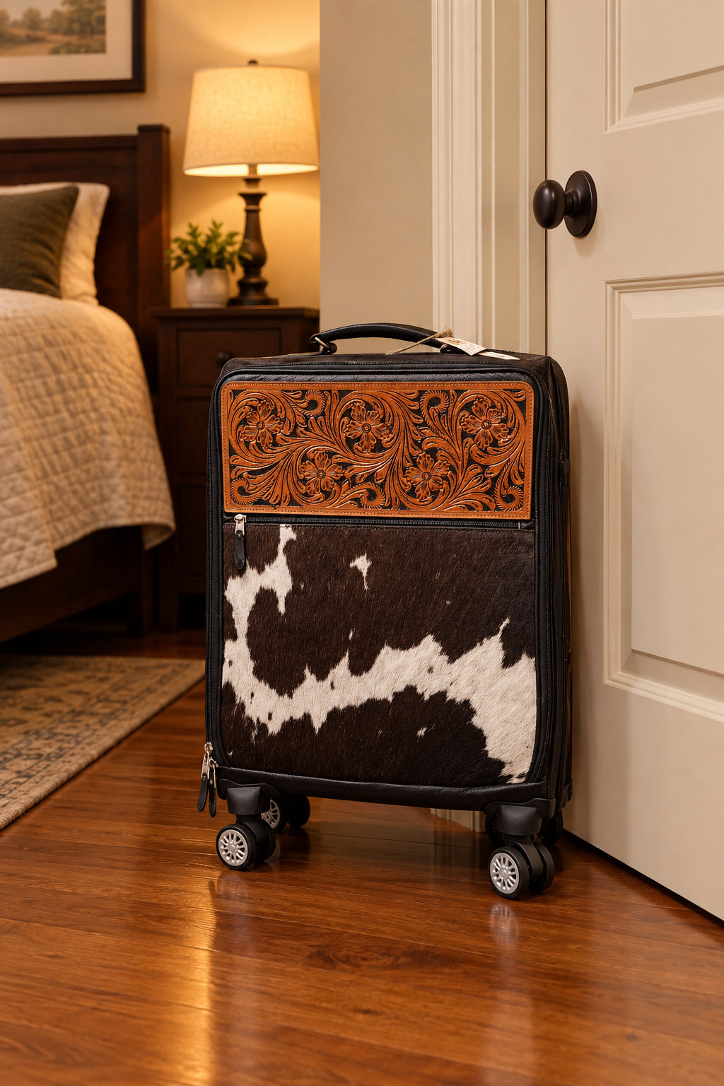 A hard-shell rolling suitcase with a decorative front panel featuring a carved brown leather floral section above a brown-and-white cowhide pattern.